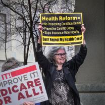 Gray haired woman holding protest sign above head asking for Health Reform