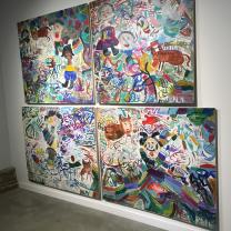 Paintings hanging on a white wall that are very large one on top of the other and of very colorful scenes