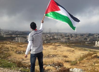 Man waving Palestinian flag on hill by big village