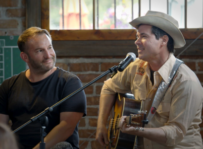 Two white guys talking one with a guitar