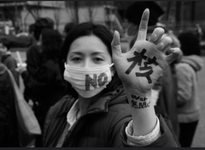 Young Japanese woman with mask on that says No and her hand says Nukes in Japanese
