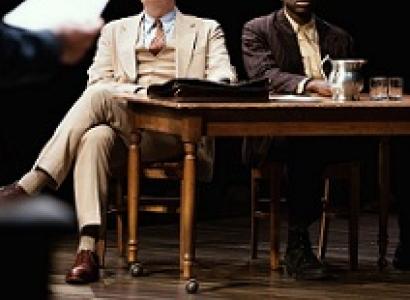 White man and black man sitting at a table looking very solemn
