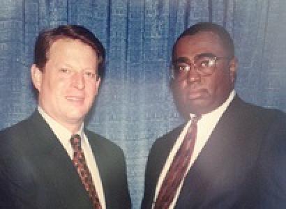 White middle aged man in a suit posing shaking hands with black man with glasses in a suit