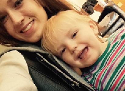 Young white woman with straight brown hair smiling and holding a blonde girl baby