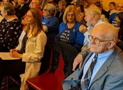 Lots of white people sitting in rows on wooden seats