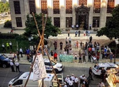 Crowd of protestors outside a big government building with a tripod looking wooden structure in the street