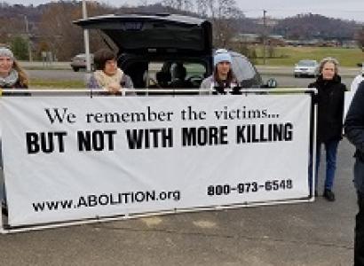 People outside holding a long white banner with black letters saying We remember the victims...But not with more killing and www.abolition.org and a phone number