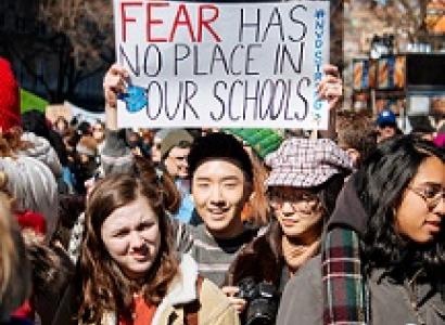 Young people wearing winter coats one young man holding a sign above his head that says Fear has no place in our schools