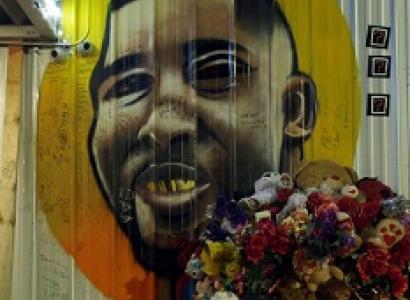 Painting of a black man's face against a yellow and orange circle on a white sided building with a bouquet of flowers in the foreground