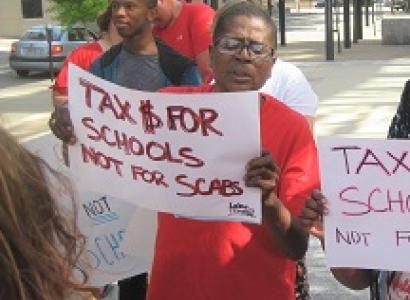 Black woman outside at rally holding a sign that says Tax $ for Schools Not for Scabs