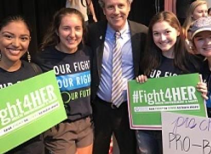 Three young women with #Fight4HER signs and one older white man in a suit