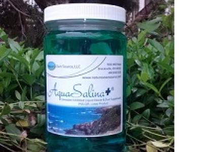 Glass looking bottle with white lid and label that says AquaSalina sitting outside in nature with grass and trees around