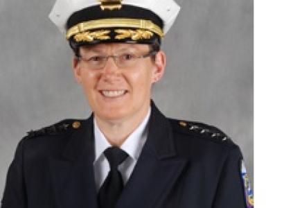 White woman in a police uniform and wire rimmed glasses smiling and posing