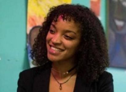 Young black woman smiling turning her head to the left wearing a black suit against a colorful wall of art