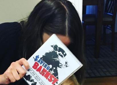Women with dark hair leaning over hiding her face with a book, Saving Banksy