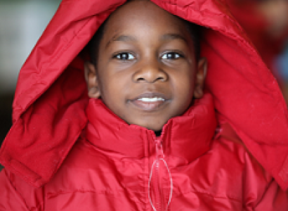 Young black child smiling and wearing a red winter coat with a hood