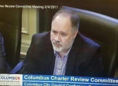 Bald man with gray goatee at a official city meeting