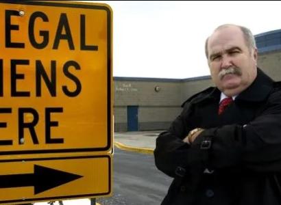 SIgn saying illegal aliens here and a stern bald older man with arms crossed and 