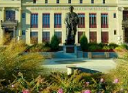 Big white government building with tall gray statue out front and some greenery in the foreground