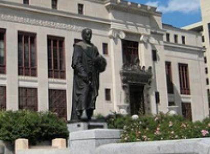 Big governmental building with statue of Christopher Columbus in front, some bushes against a blue sky with white clouds