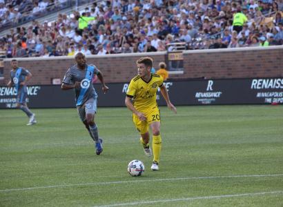 Two soccar players on the field on opposite teams, one in blue and one in yellow kicking the ball