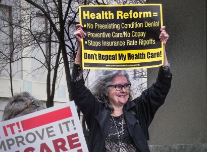 Gray haired woman holding protest sign above head asking for Health Reform