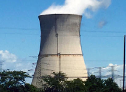 Big fat nuclear plant smokestack with white smoke billowing out against a blue sky