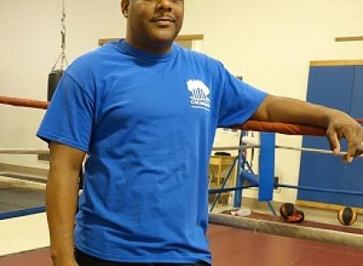 Black man in blue t-shirt standing next to a boxing ring