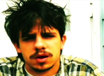 Close up of a young white man's face with dark hair askew and a moustache and goatee