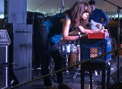 Dark haired woman leaning over a keyboard with a band on a stage