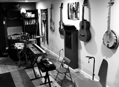 Black and white photo of room with lots of guitars and a banjo hanging on the wall and other musical instruments