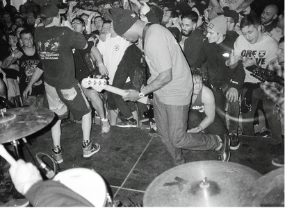 Black and white photo of black guy playing guitar with people all around dancing