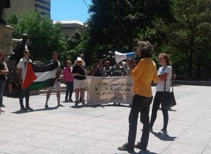 Man speaking into bullhorn and crowd with Jewish Voices for Peace sign