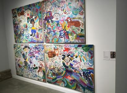 Paintings hanging on a white wall that are very large one on top of the other and of very colorful scenes