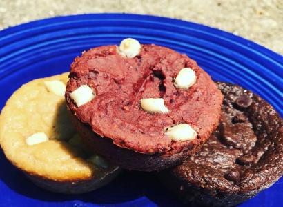 Cupcake-looking desserts, round, each one a different color, yellow, brown and dark brown with white chocolate chips on a blue plate