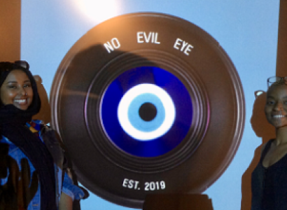 Black woman standing next to a large film reel that says No Evil Eye on it