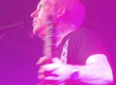 Purple lighted picture of white man performing side view holding a guitar