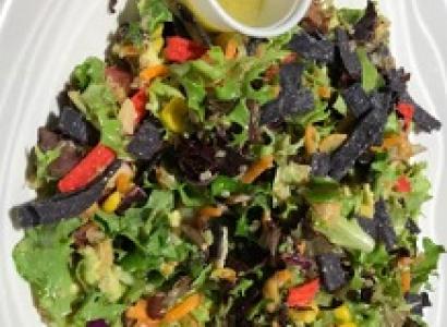 Salad on a plate with a little cup of salad dressing at the side