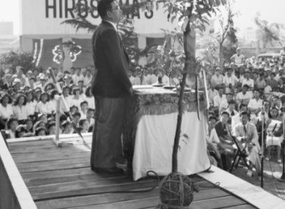 Guy at a platform speaking to a crowd with sign No More Hiroshimas