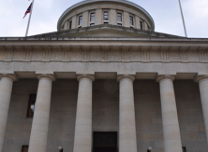 Big white government building with columns and a round top and  flags flying on each side