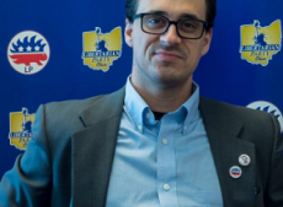 White man with black rimmed glasses in a suit coat