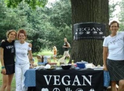 Three happy people by a table outside that says VEGAN on a sign