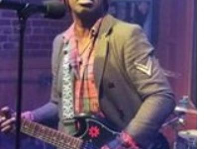 Black man in a hat playing a guitar at a mic