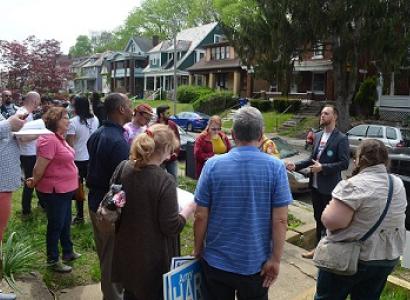 A group with a variety of black and white, old and young people standing outside in a neighborhood with trees and houses