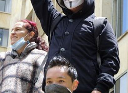 Guy wearing anonymous Guy Fawkes mask with fist in air at protest with others 