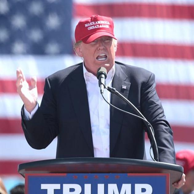 Trump in front of flag with red baseball cap on