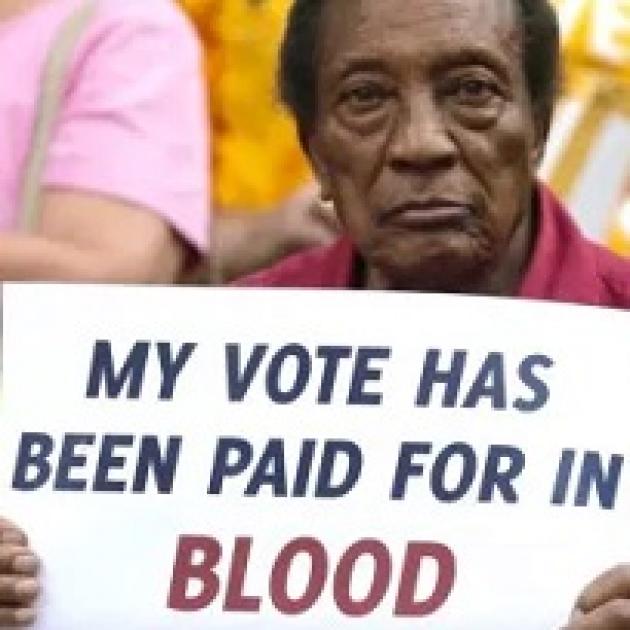 Black man holding a sign reading My vote has been paid for in BLOOD
