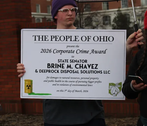 Protester holding corporate crime award for Senator Chvaez