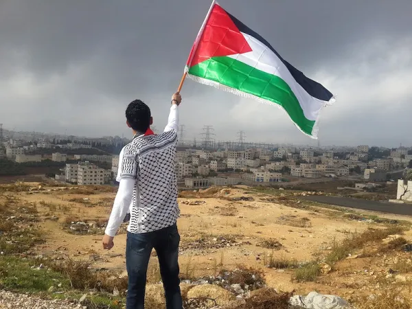 Man waving Palestinian flag on hill by big village
