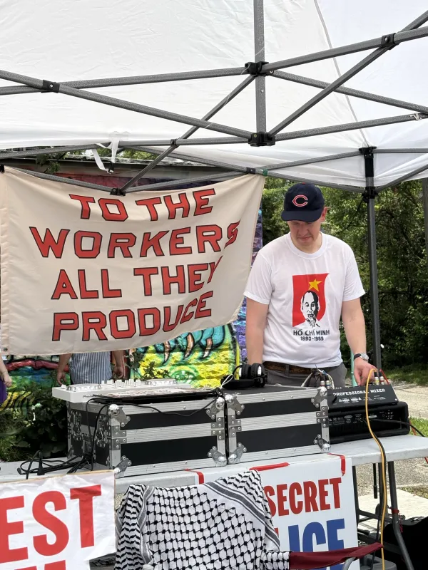 Man at table with sign saying To The Workers for all they Produce